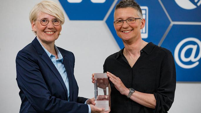 Zwei Frauen halten gemeinsam einen Pokal und lächeln in die Kamera.