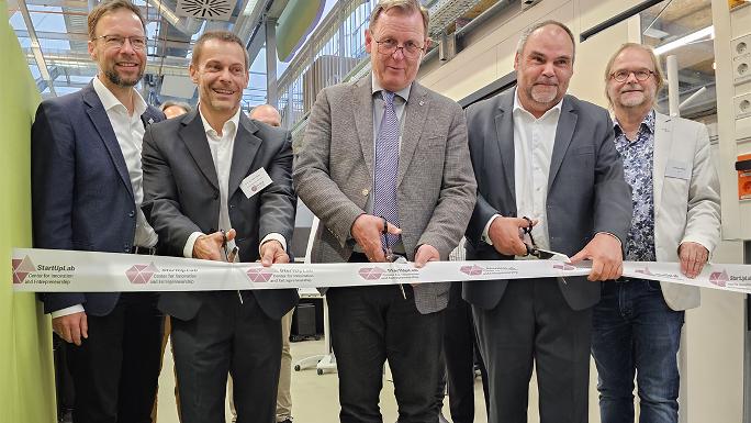 Fünf Männer stehen in einer Reihe. Die drei in der Mitte halten Scheren in den Händen und zerschneiden gerade ein Absperrband.