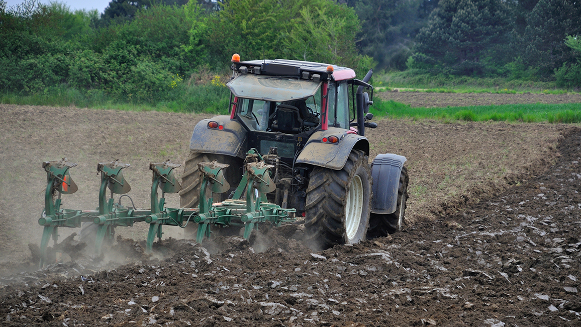 Ein Traktor pflügt ein Feld, fotografiert von schräg hinten.