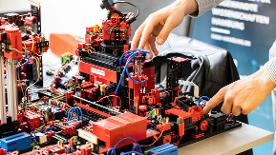 Eine komplexe Maschine aus Legoteilen, zwei Hände bedienen Knöpfe