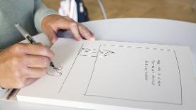 Eine Person zeichnet etwas auf ein Blatt Papier