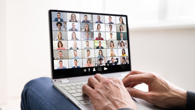 A laptop with faces in a video conference, two hands on the laptop keyboard