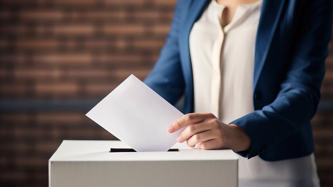 A ballot box with a person behind it who is just pushing a ballot paper into the slot.