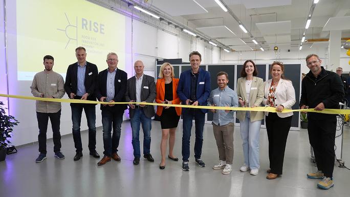 About 10 people stand in a row in front of an opening ribbon and are about to cut it.